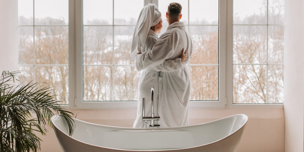 couple standing in front of bathtub looking out window